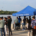 People stand around a blue tent with the words "Wascana Centre: on it. They are by a lake.