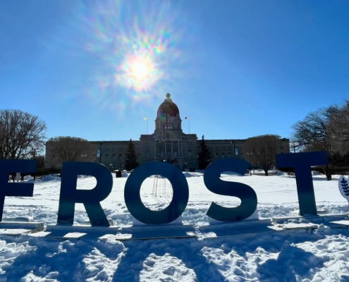 Giant letters spell out "FROST", with the Saskatchewan Legislative Building in the background.
