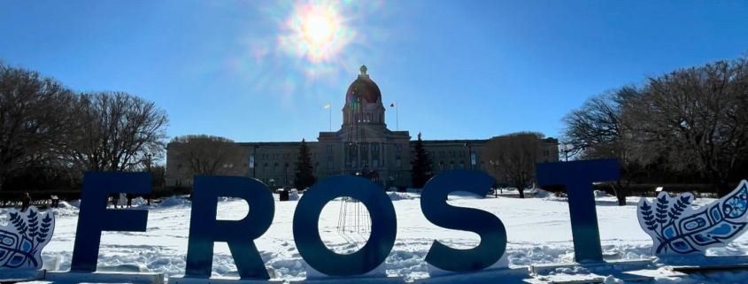 Giant letters spell out "FROST", with the Saskatchewan Legislative Building in the background.