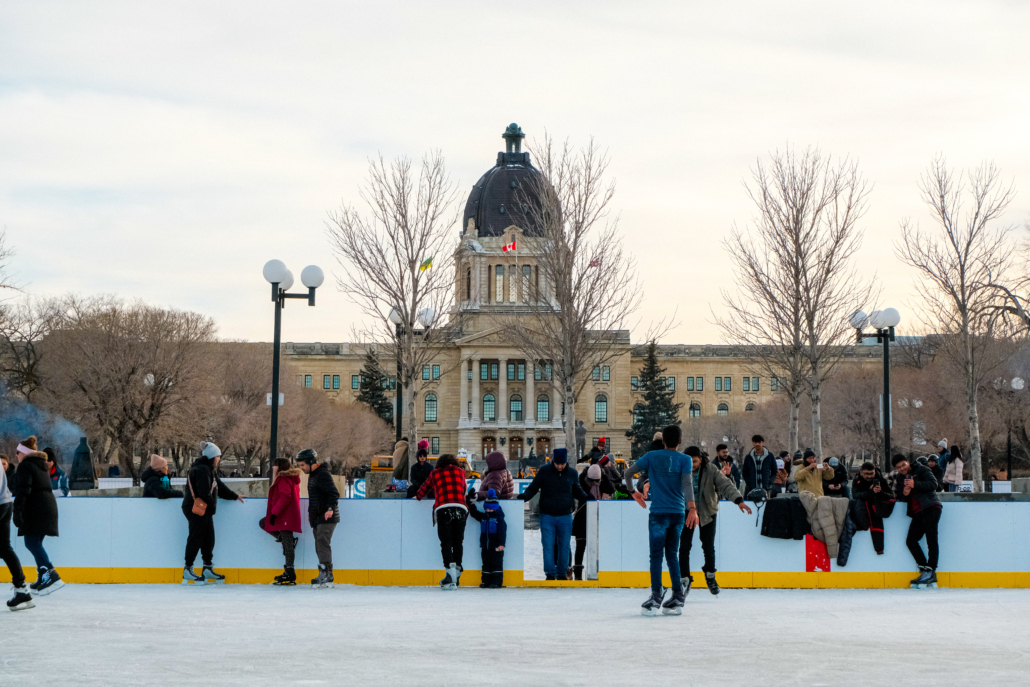 People ice skating on an outdoor rink in front of the Saskatchewan Legislative Building.