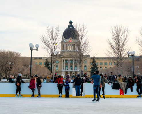 People ice skating on an outdoor rink in front of the Saskatchewan Legislative Building.