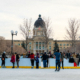 People ice skating on an outdoor rink in front of the Saskatchewan Legislative Building.